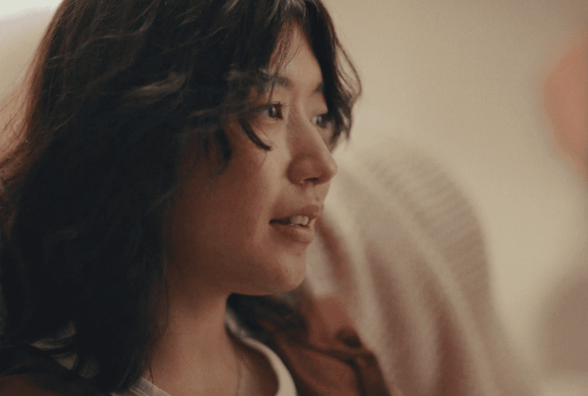 Person with long hair sitting on a couch, looking to the side.